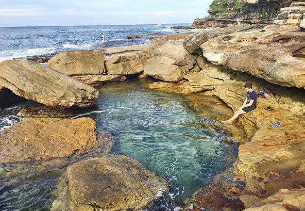 In Australia, a boy sitting on the rocks at the oceans edge