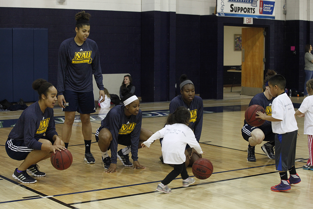 A young girl tries dribbling with members of the NAU women's basketball team