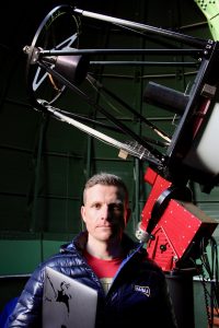 Colin Chandler stands in front of a telescope.