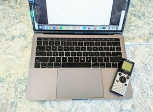 A handheld tape recorder sits on a laptop.