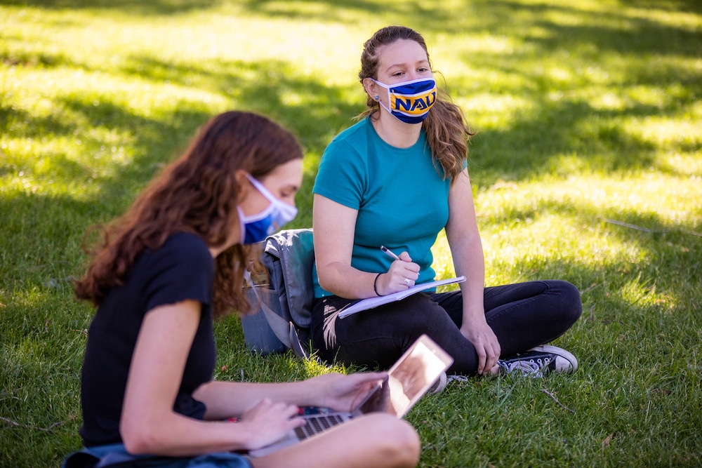 Two masked students sit in grass