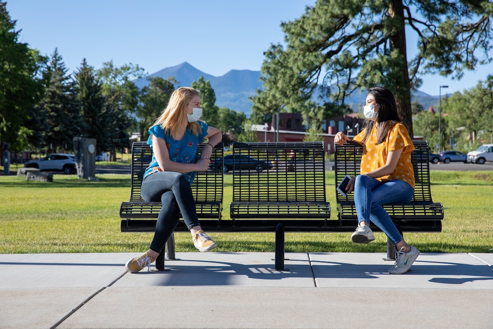 Two masked students sit on bench