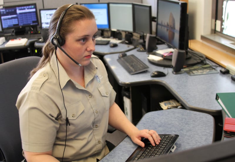 A female dispatcher wearing a headset sits at a computer.
