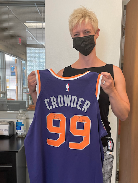 Heather Thomas stands in office and holds up Crowder jersey