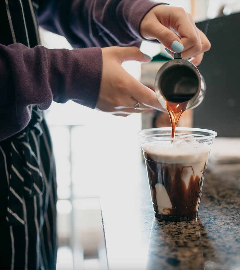 Barista pours shot of espresso into cup of milk and chocolate