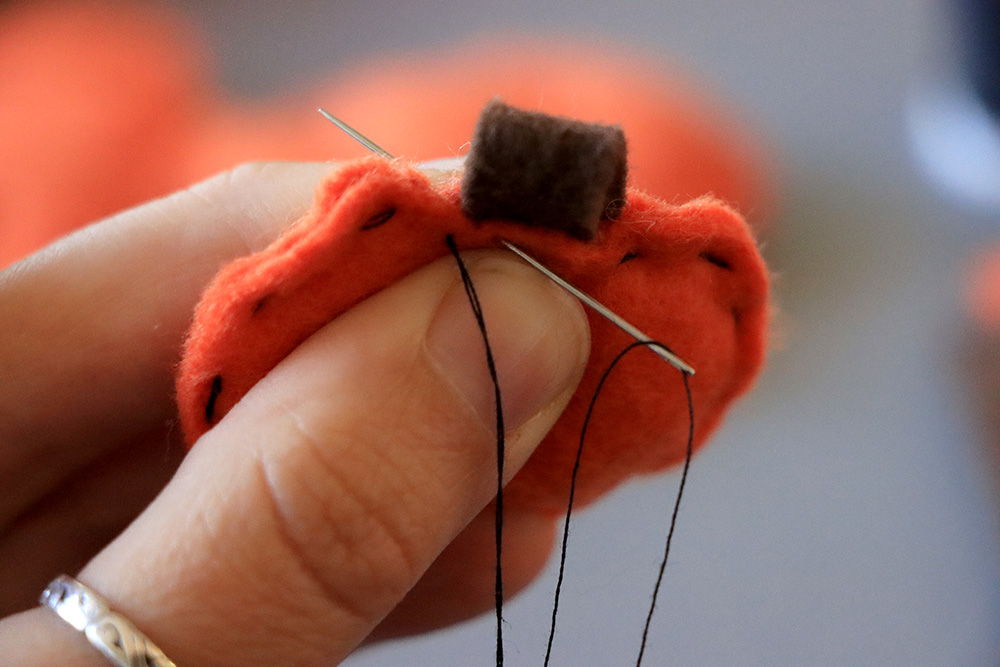 Needle stitches on brown stem to pumpkin