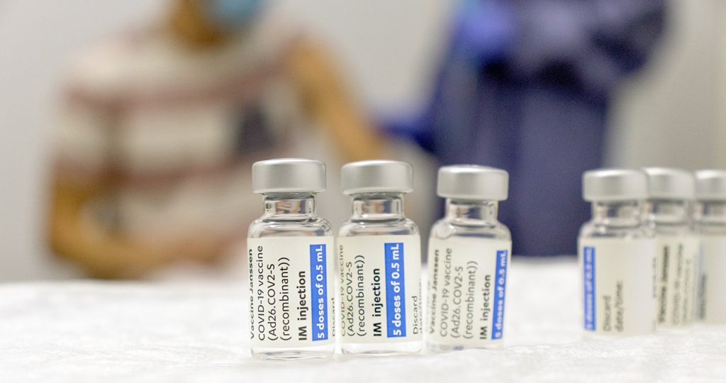vaccine vials sit on table with patient and doctor in background