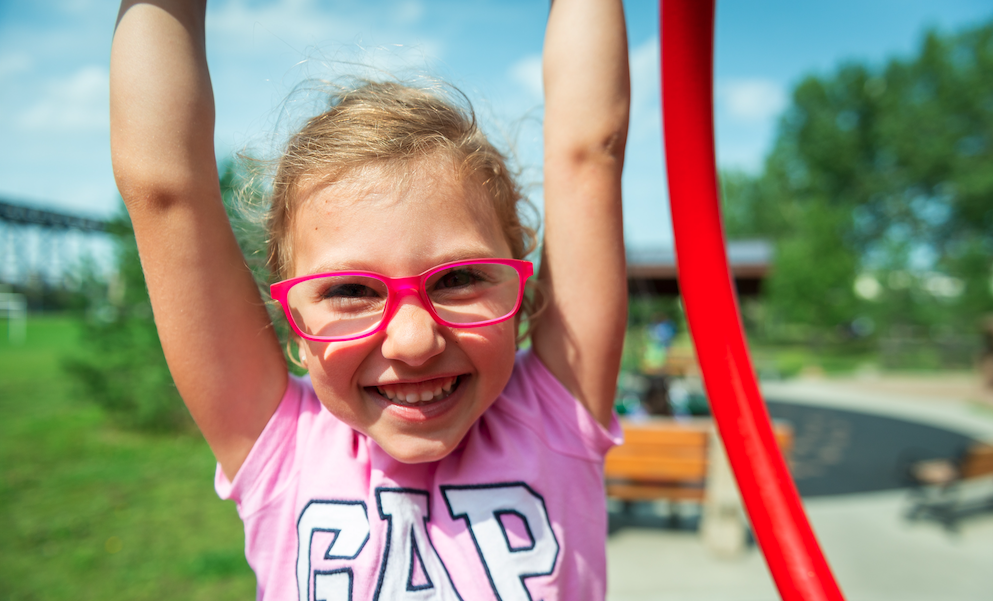 Girl wearing glasses hangs from jungle gym