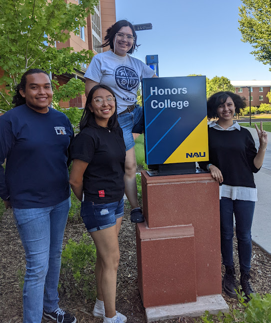 Four students stand around the Honors College sign