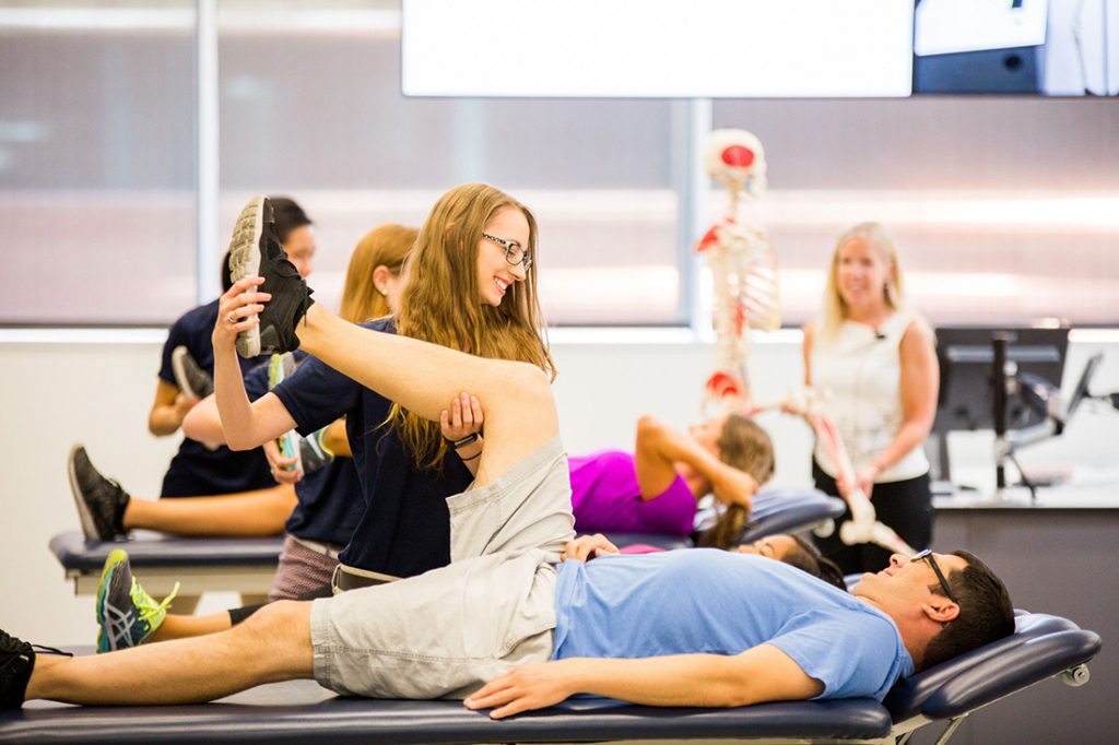 A physical therapy student helps a patient lying on a table stretch.