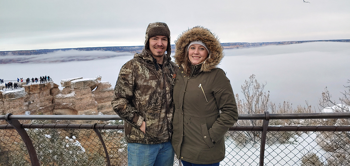 Tyler and Amanda Derzay in winter coat in front of the foggy Grand Canyon