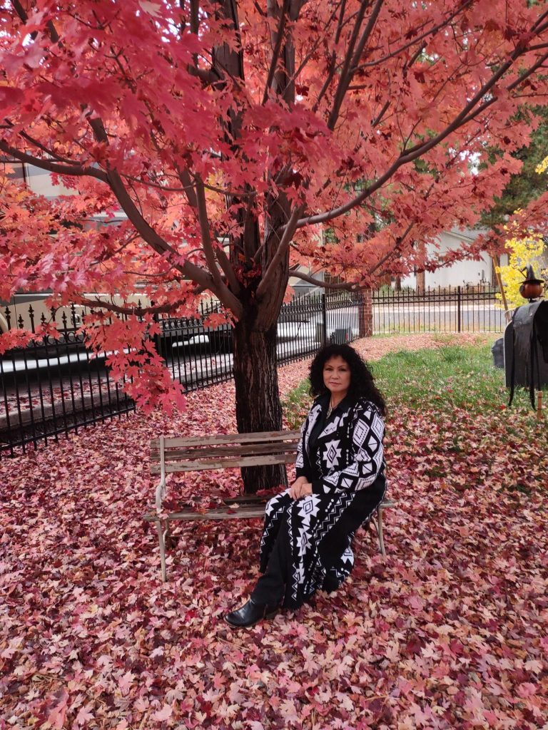 Sharon Moses sitting on a bench amid red leaves a bench