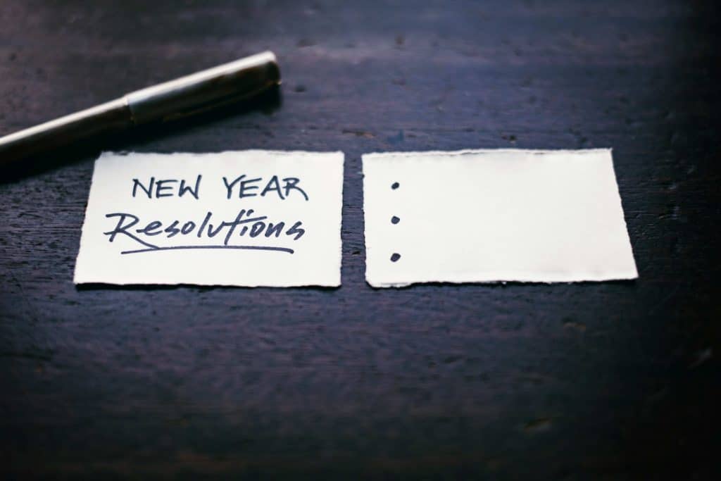 two smalled pices of paper wth pen sitting above them. 'New Year Resolutions' written on left piece of paper and three bulleted list with no text.