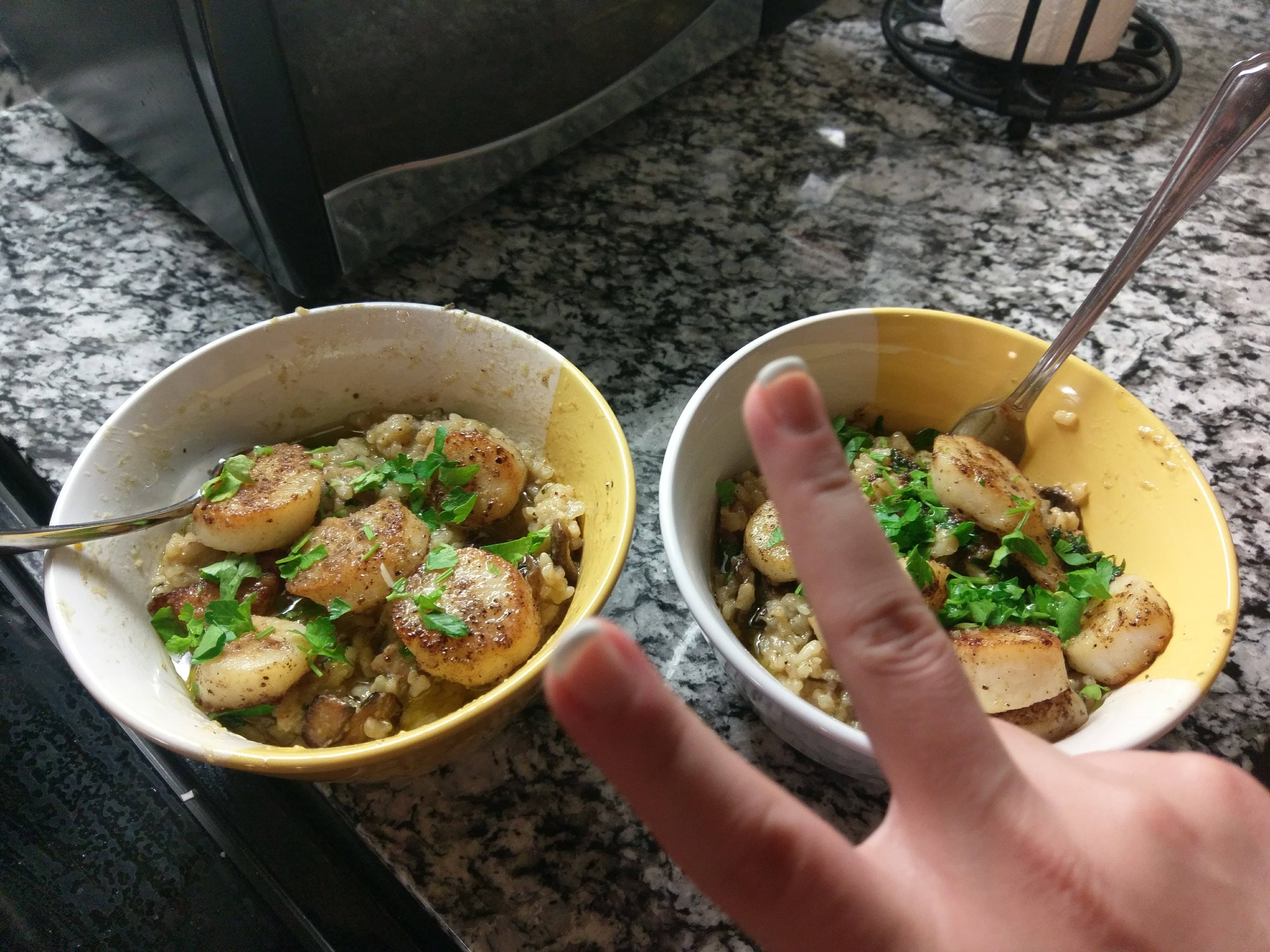 two white and yellow cereal bowls filled with risotto and topped with scallops