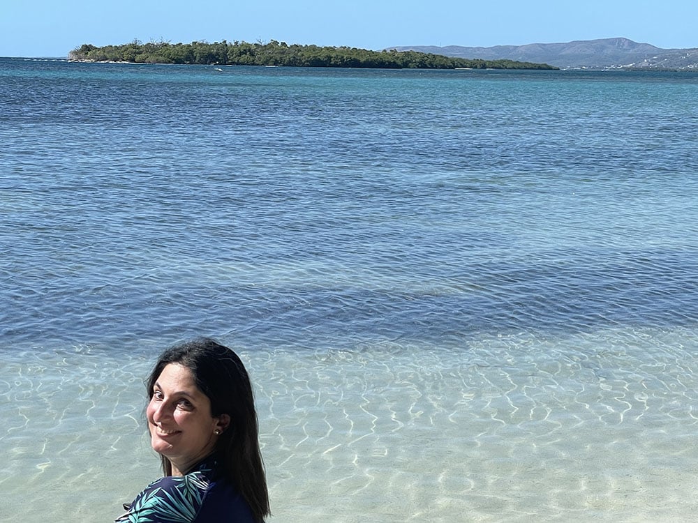 Rima Brusi sitting at the edge of the ocean in Puerto Rico
