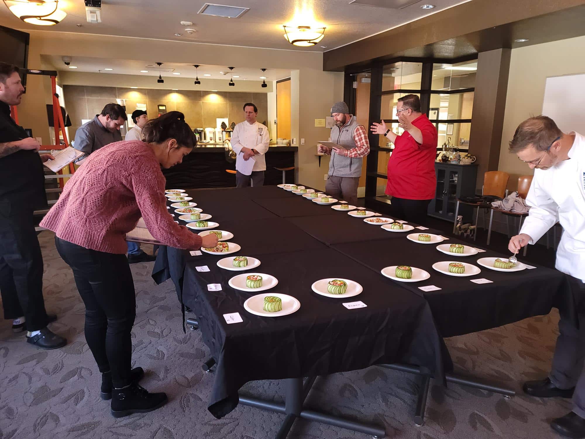 Judges around a black tables with all the salads to taste, critique and judge.