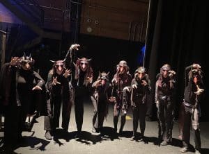 The Cast of NAU Lyric Theatre Mozart's Don Giovanni with live opera movie, in masks, dressed in all black, which arms ouout and hands extended 