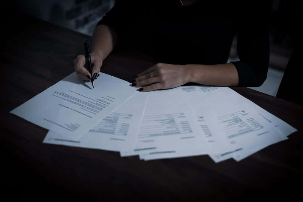 Person with black nailpolish holding pen working on a bunch of paperwork