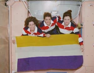 Three woman astronauts holding a flag