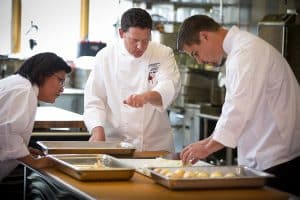 Two chefs and a student, all in chef's whites, work in the NAU kitchen.