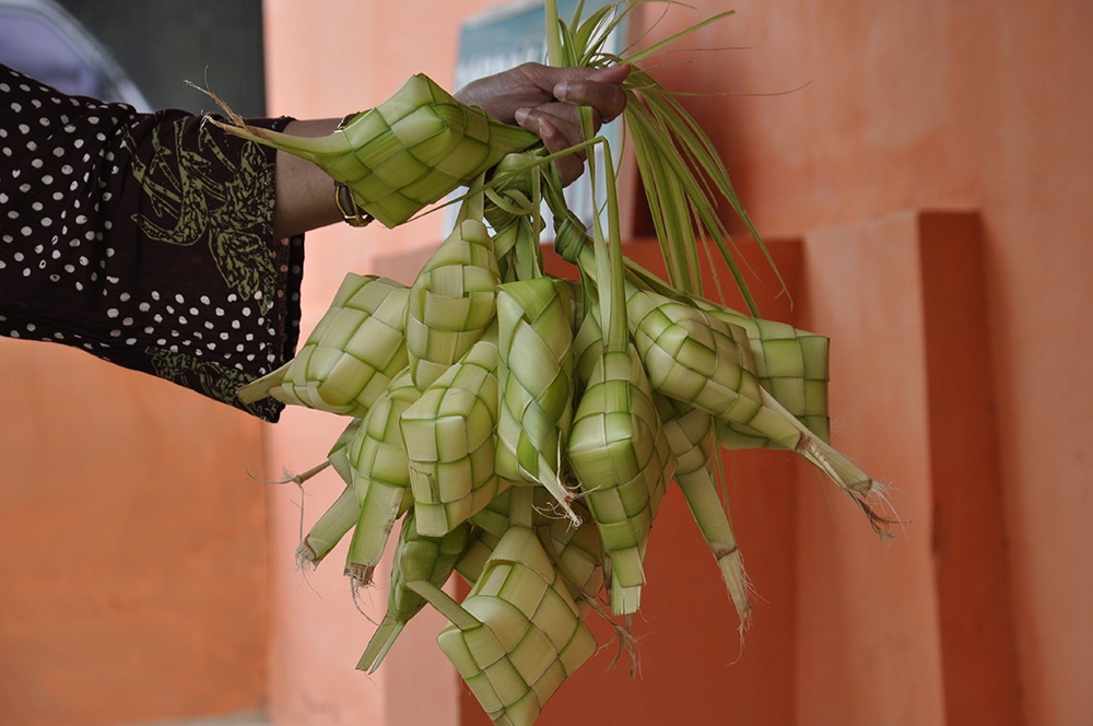 A woman holds ketupat, diamond shaped containers woven from strips of palm leaves