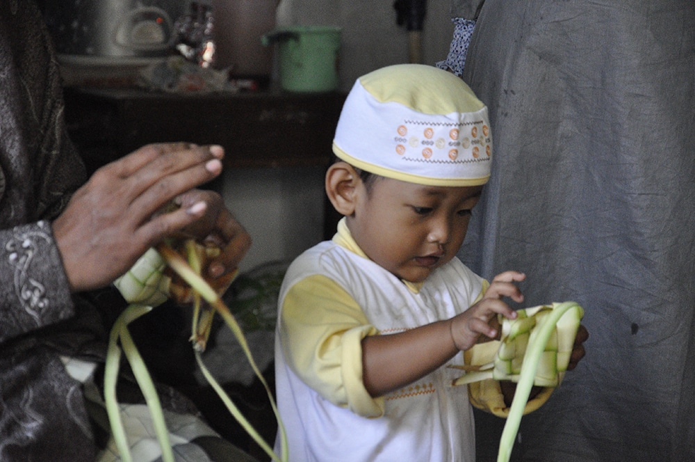 A young boy weaves ketupat out of palm leaves.