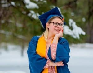 Rebekah Wucinich in her cap and gown with a snowy forest behind her.