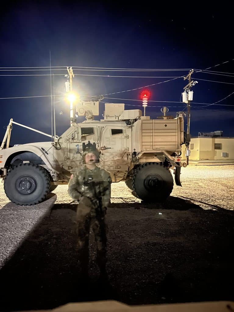 Harmon posing in aArmy gear in front of a tank