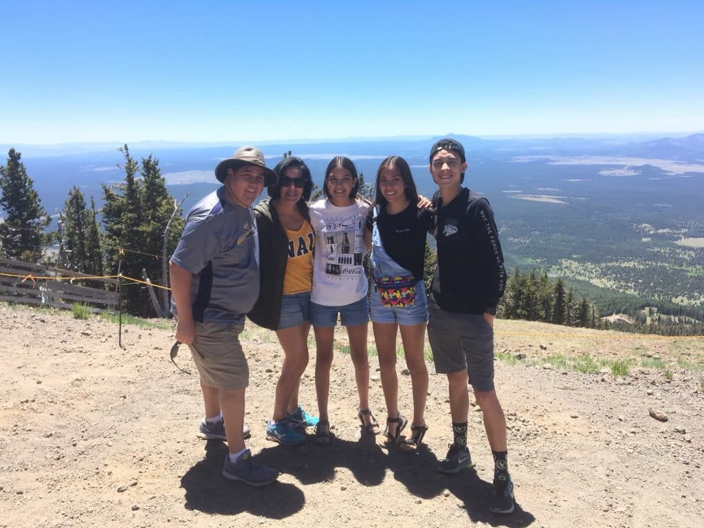 Patty Diaz and her family stand on a trail on top of a mountain with blue sky.