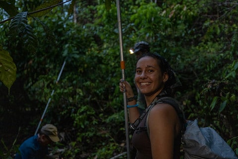A woman looks at the camera while doing work in the jungle at night.