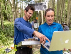Mariah Carbone and Austin Simonpietri working on a laptop in the forest.