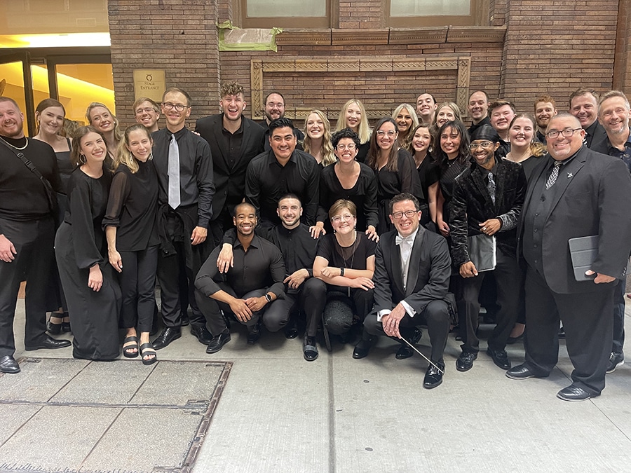 Twenty people in black clothing pose at Carnegie Hall