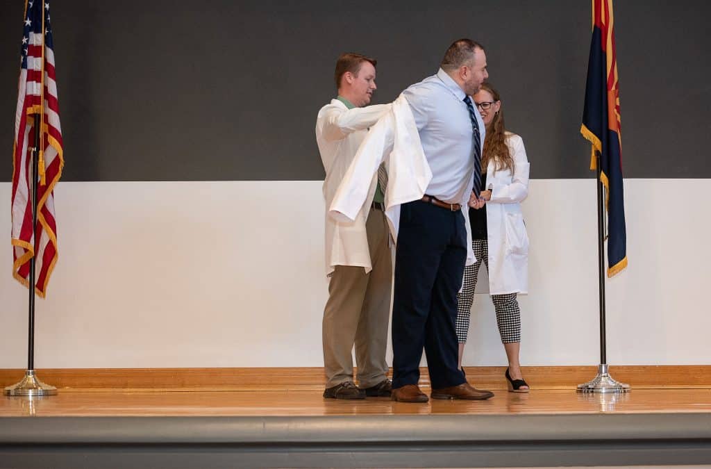 A man and a woman put a coat on a future physician assistant.