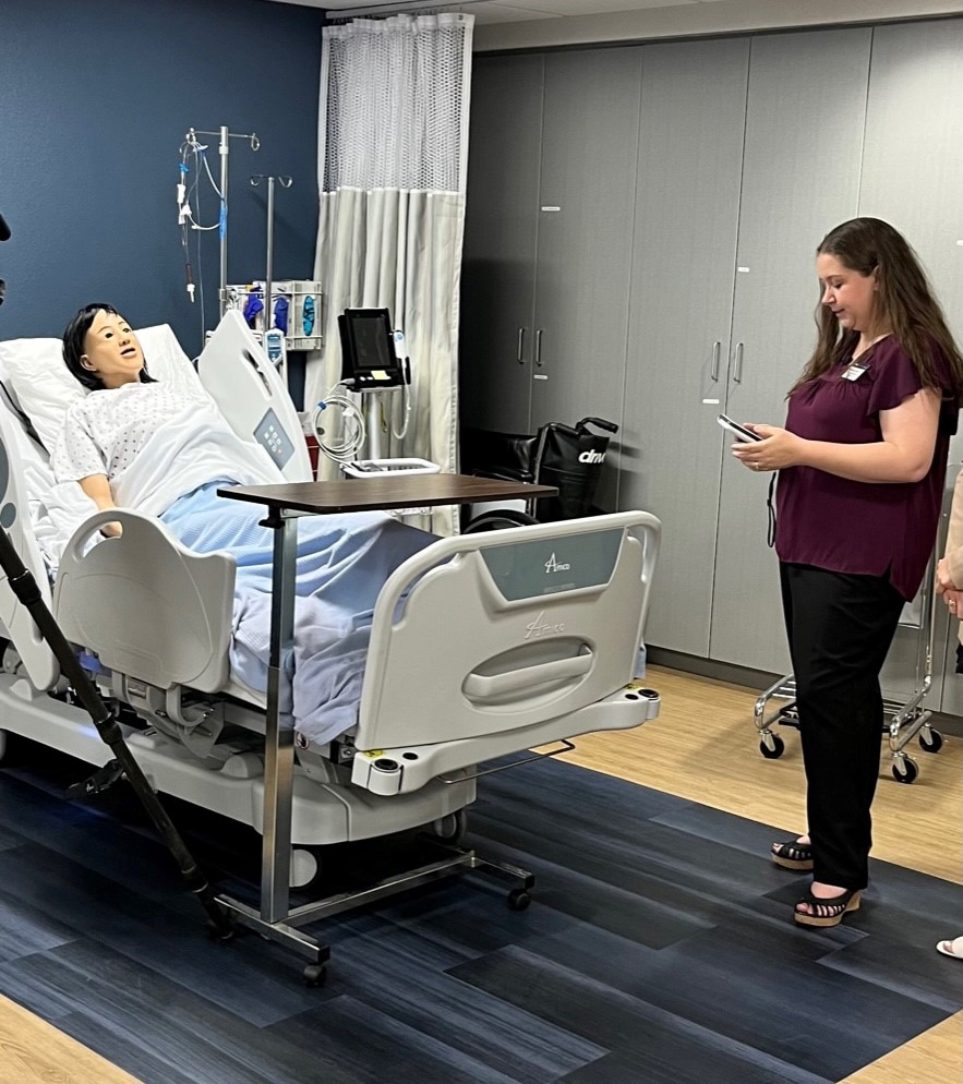 A nursing faculty member stands by a bed with a lifelike manikin, which students use to practice their nursing skills.