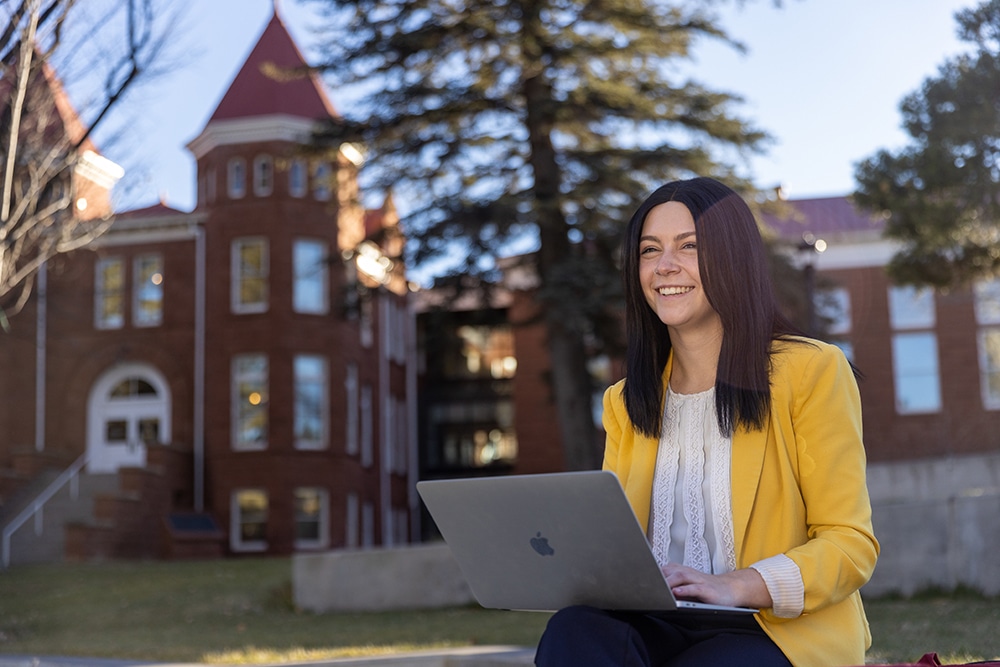 Rachel Kanyur sitting in front of Old Main with a laptop