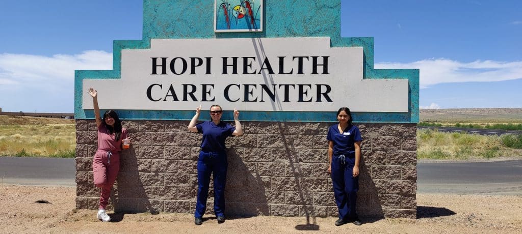 Three students in scrubs stand in front of the Hopi Health Care Center