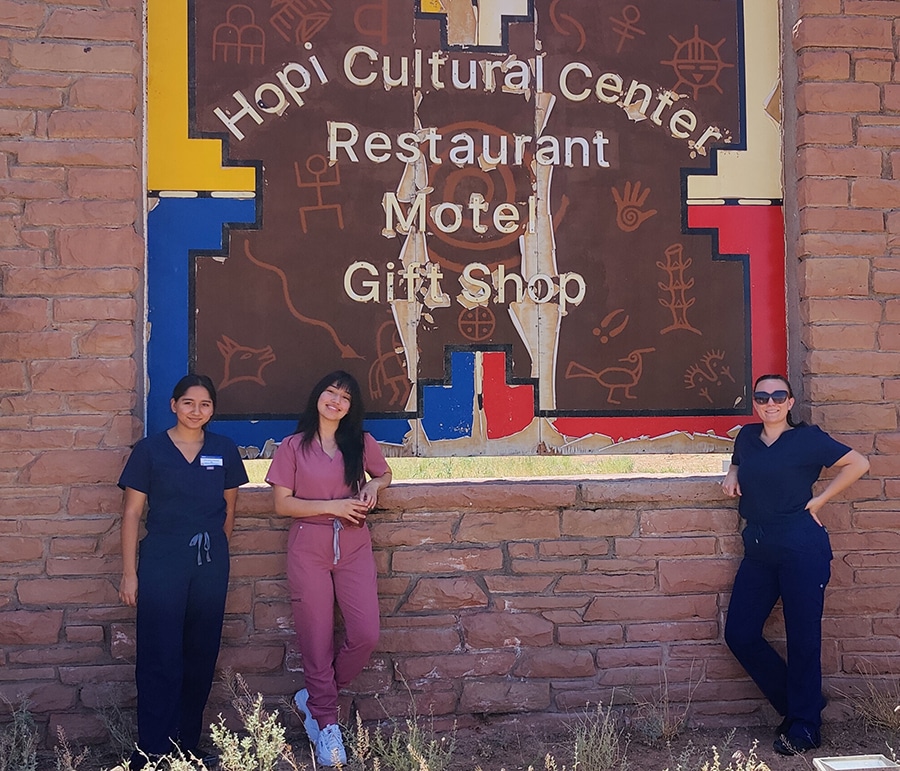 Three students stand in front of the Hopi Cultural Center sign