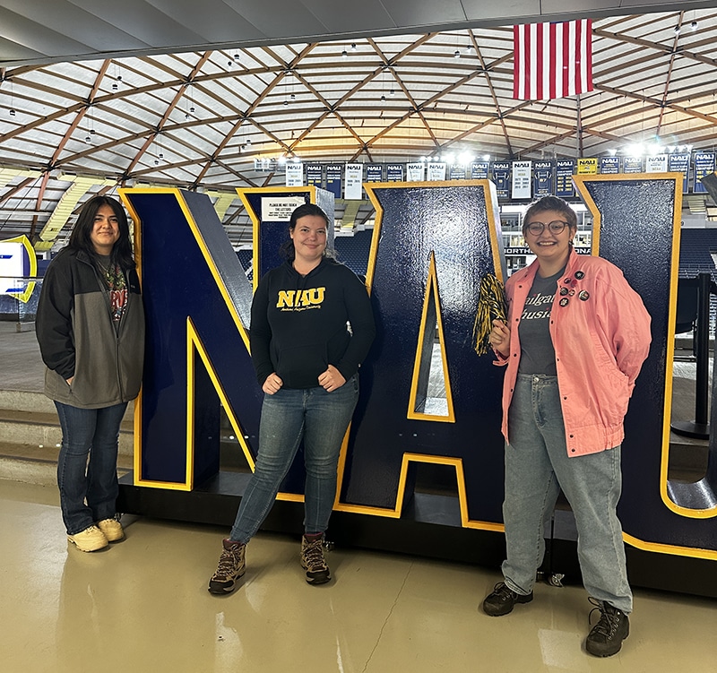 Three people stand in front of an NAU sign at the Skydome.