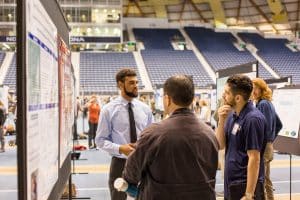 Young man at symposium showcasing his research to two people