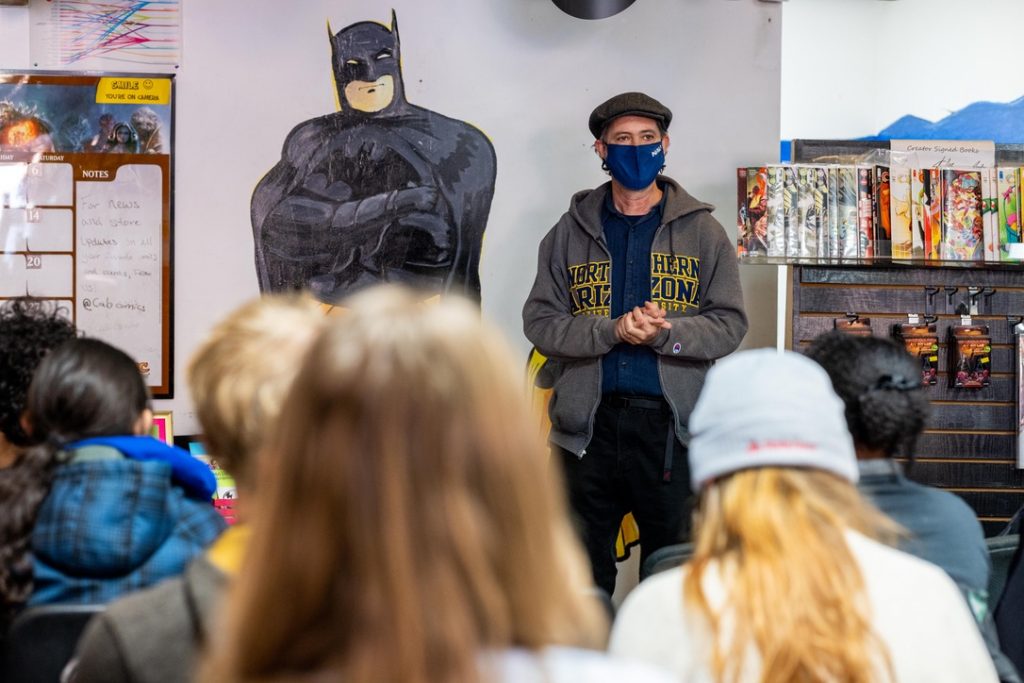 Robert Wallace next to a Batman poster talking to a class