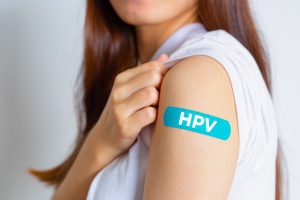 Closeup of a woman raising her t-shirt sleeve to show a bandage with HPV written on it
