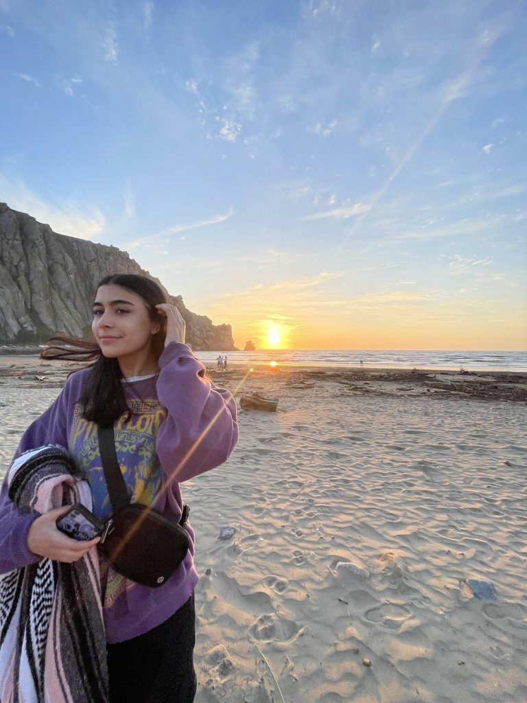 Cecilia Perez standing on a beach at sunset and looking into the distance 