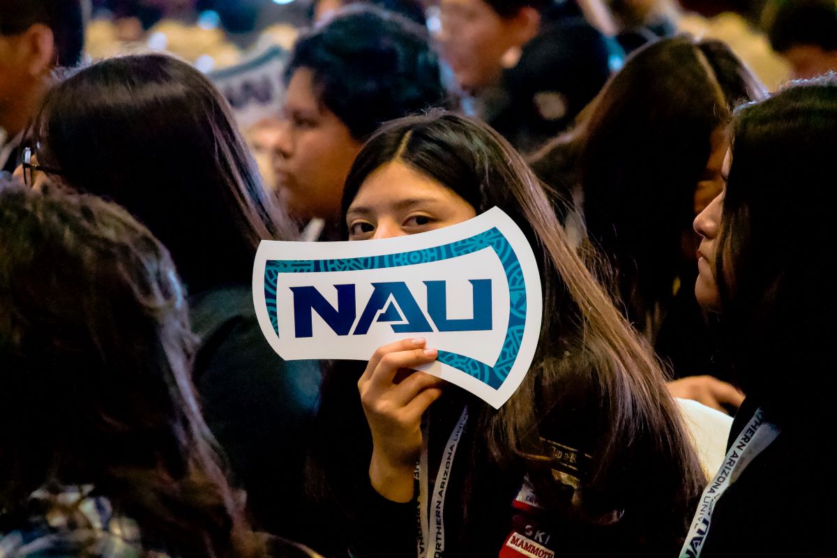 Long haired Indigenous girl holding NAU axe logo up in front of the bottom of her face