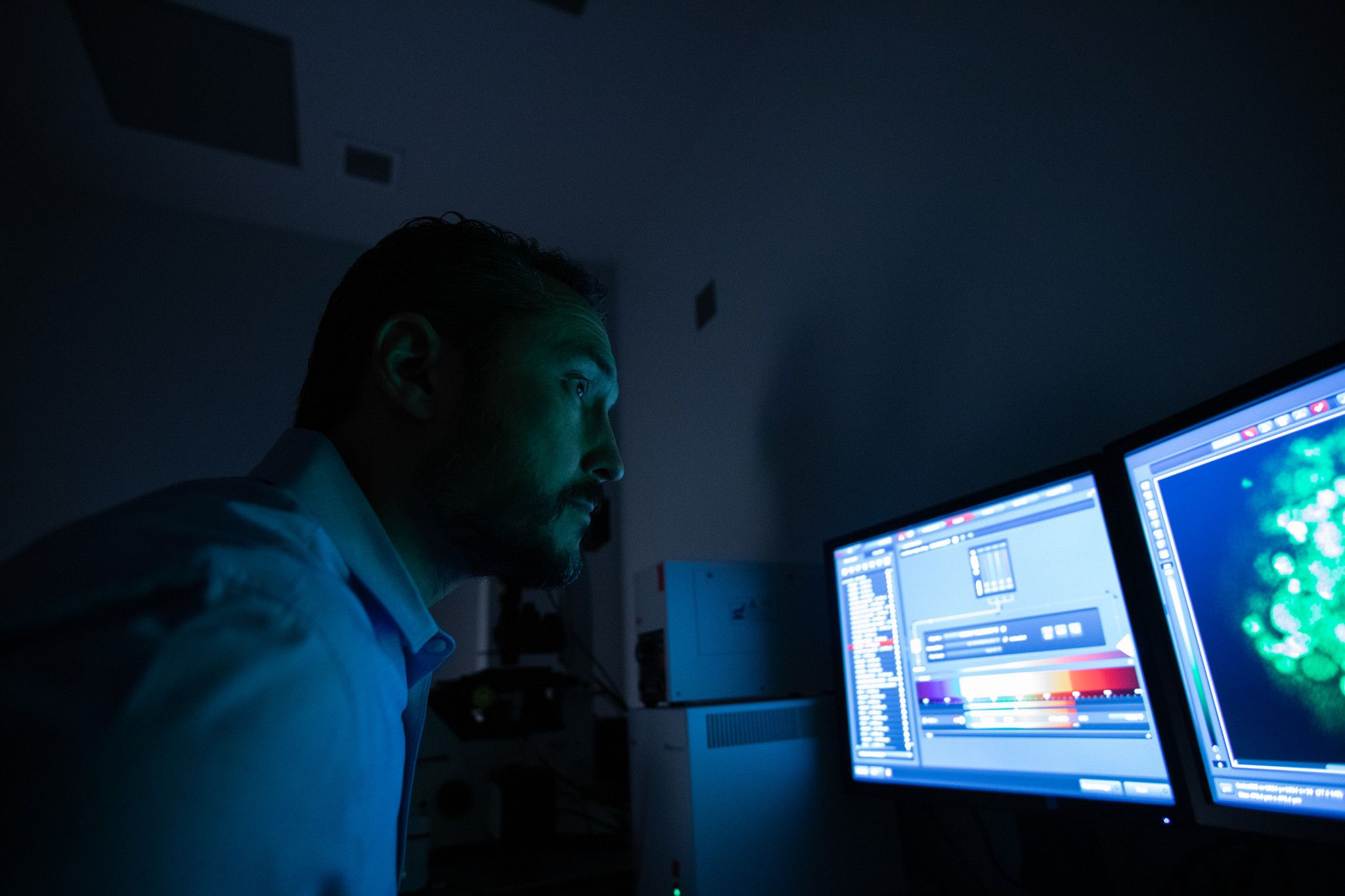Robert Kellar in a dark room looking at a computer screen that casts a blue glow over him and the room