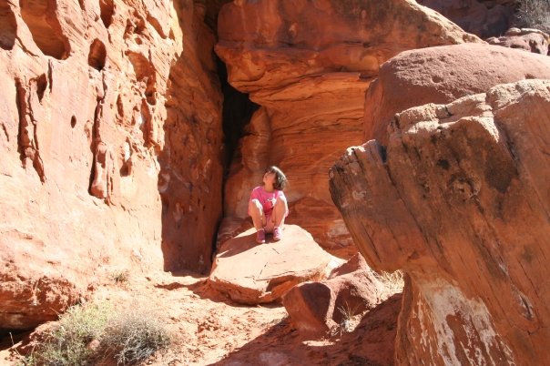 Sydney as a child crouched on a slab of red stone and looking up at the taller red rocks surrounding her