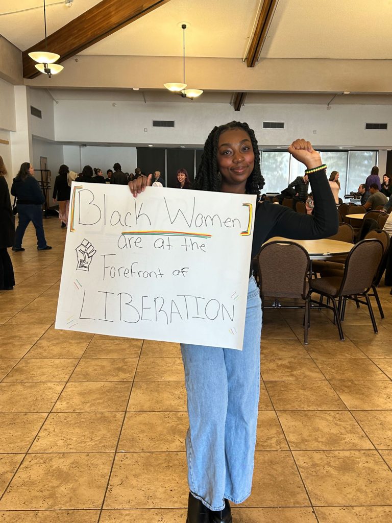 Cassie Bonah holding up a poster that reads "Black women are at the forefront of liberation" and raising one fist in the air