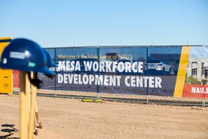 Construction banner that reads "Mesa Workforce Development Center" with hard hat hung on shovel handle in the foreground.