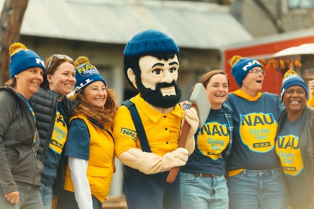 NAU employees wearing university branded T-shirts and hats posing with Louie the Lumberjack outside