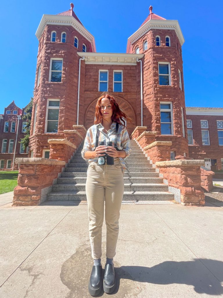 Victoria Wiley holding binoculars in front of Old Main on the NAU campus