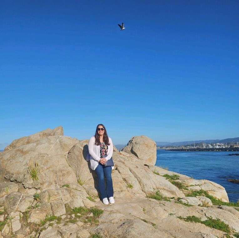 Marcy Hurtado on a rock overlooking the ocean and blue sky.
